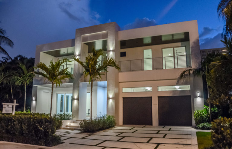 Modern luxury mansion at dusk with illuminated pool and tropical landscaping